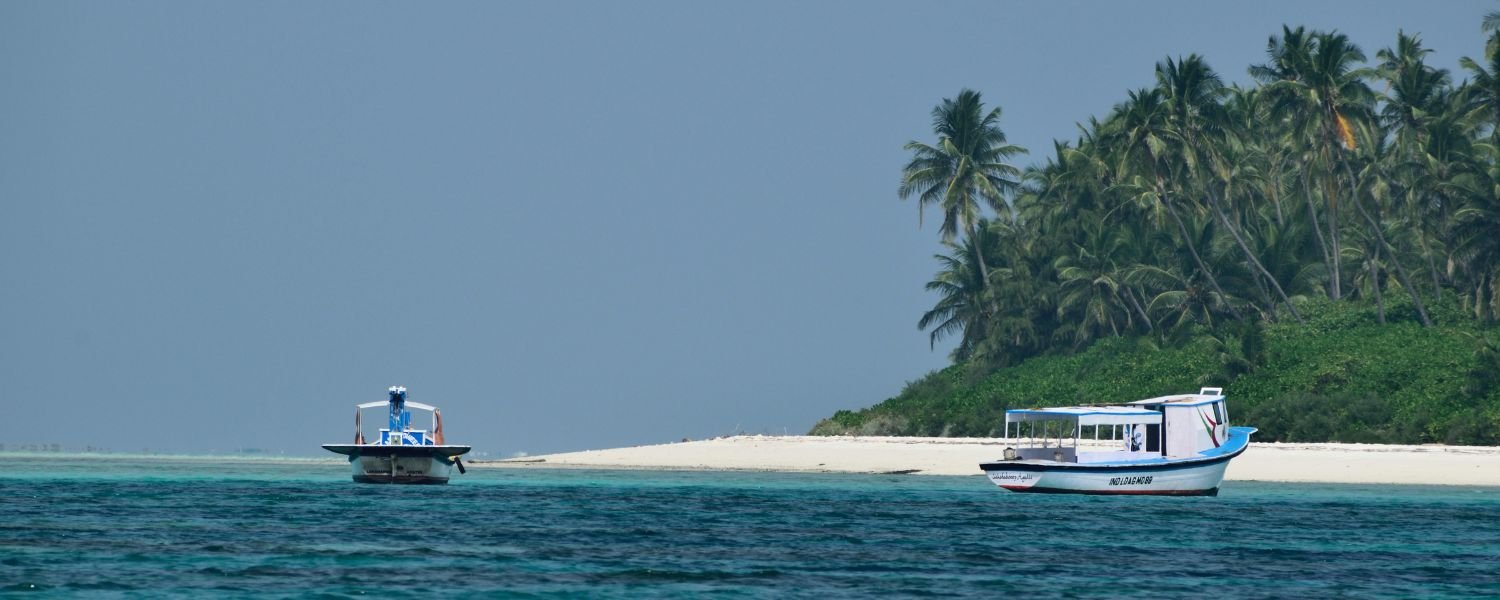 Lakshadweep beach with palm trees and fishing boats on clear blue sea